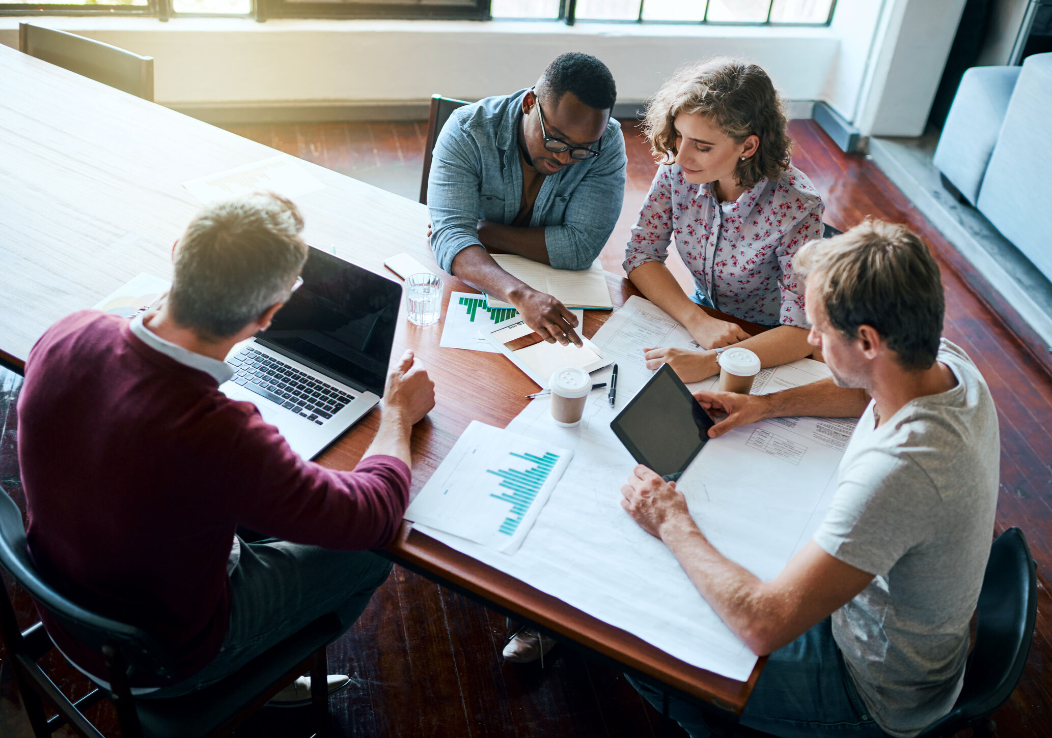 Group of people sitting at an office desk working on a laptop and tablet. 